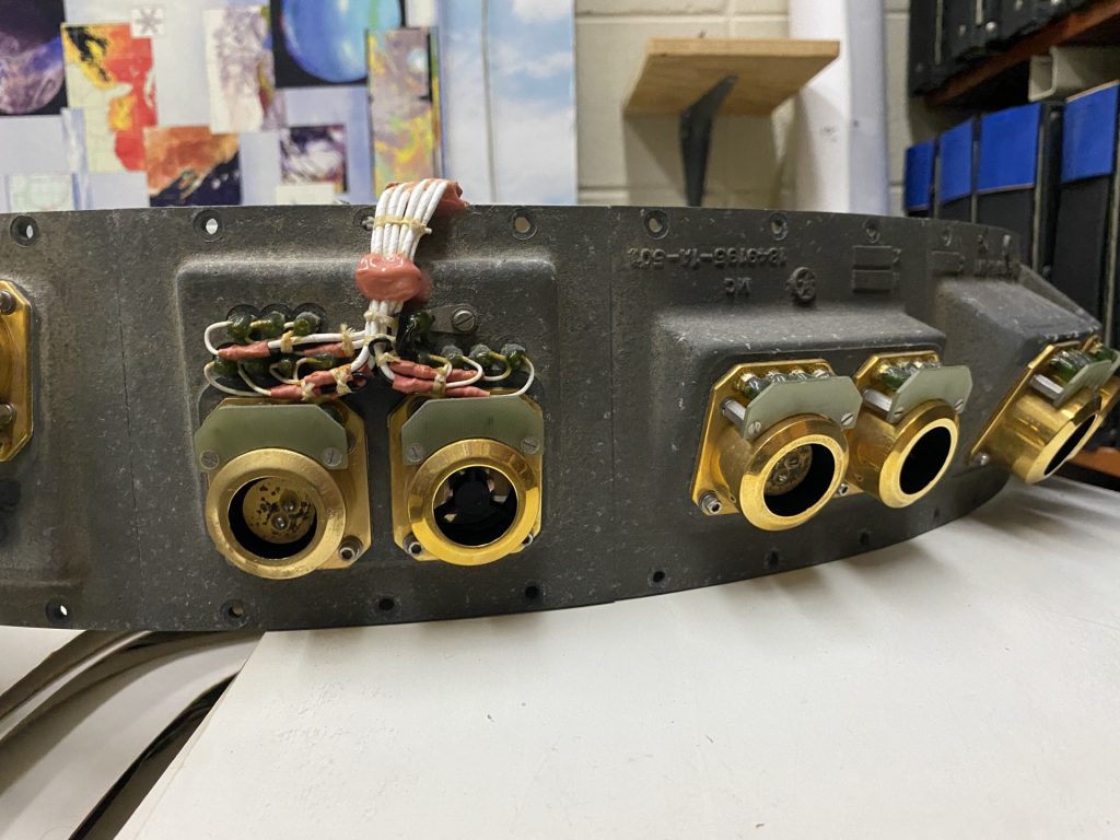 A long, curved piece of metal with various gold tubes attached, along with wires adhered to the metal with a pink substance.