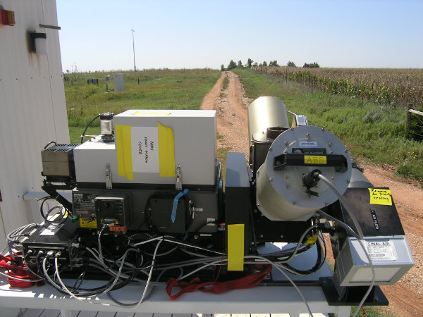 An array of sensors connected with wires sits on a table in a field, pointed at the clear, blue sky.