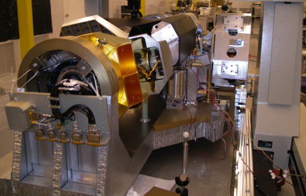 A bulky, metal piece of equipment fills a room, wires running from all ends and connecting it to various external electronics.