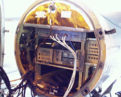 A tube-shaped instrument, open on one end, is filled with electronic components, gold foil, and wires. 
