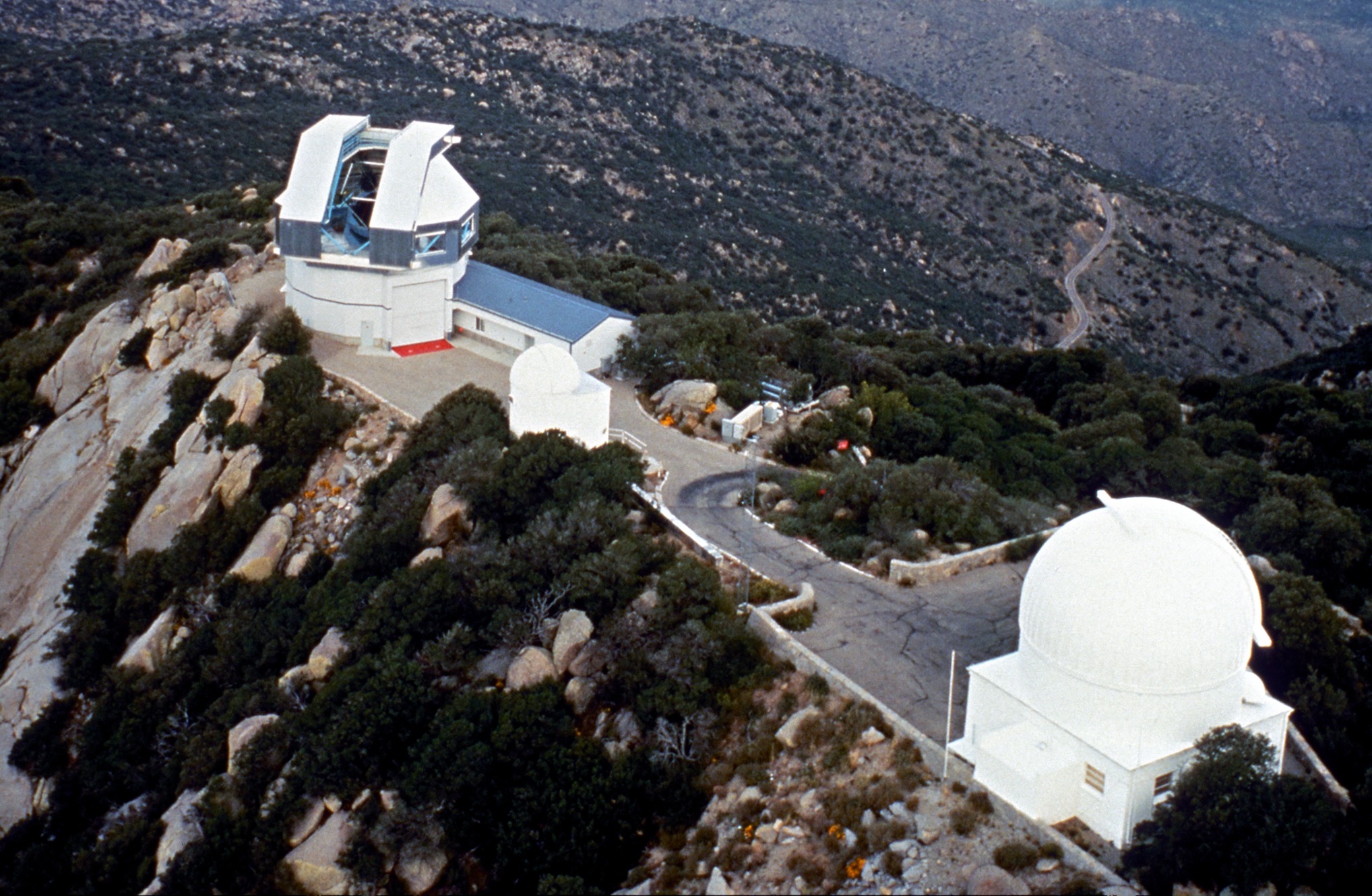 A domed observatory sits atop a rocky peak overlooking a dry, rocky landscape.