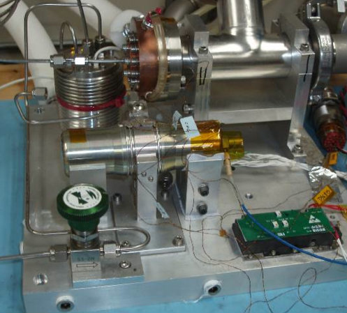 An array of small metal components sit on a workbench, wires connecting knobs to electronics to circuit boards.