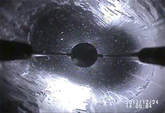 A flashlight illuminates a deep, icy borehole, the light catching on particles floating in the water. 